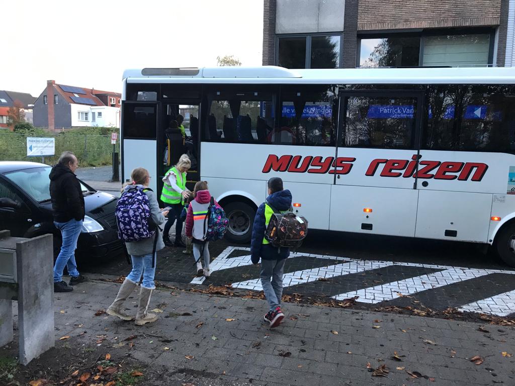 een aantal kinderen stapt op de schoolbus, de busjuf ontvangt hen 